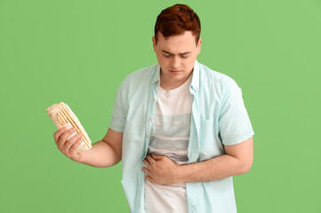 Young man with stomachache holding doner kebab on green background