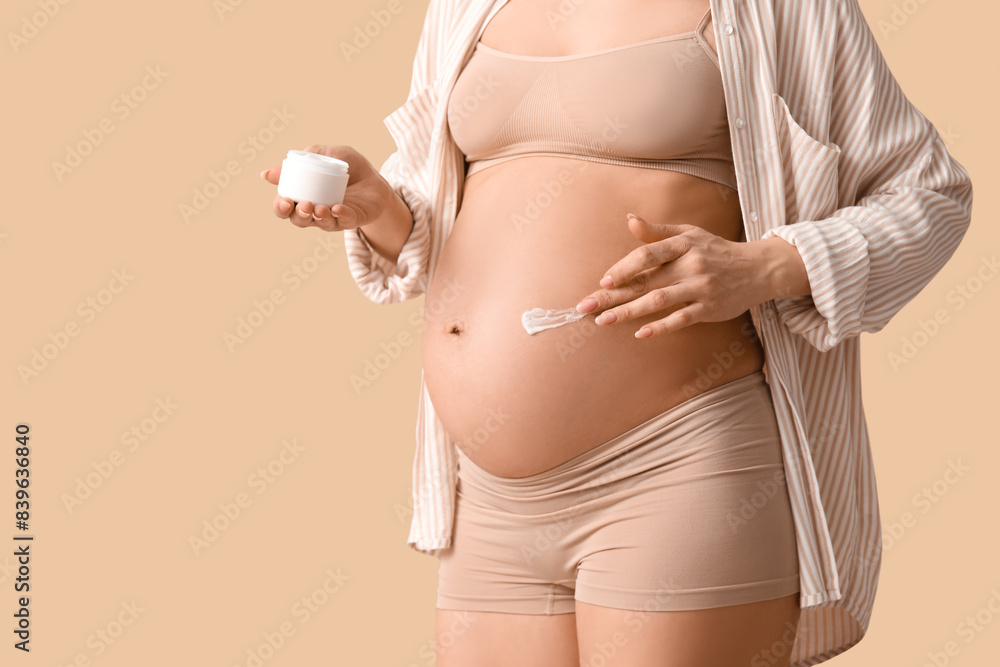 Wall mural Young pregnant woman applying cream against stretch marks on beige background