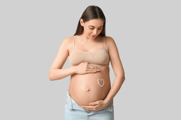 Young pregnant woman with heart made of cream on her belly against grey background