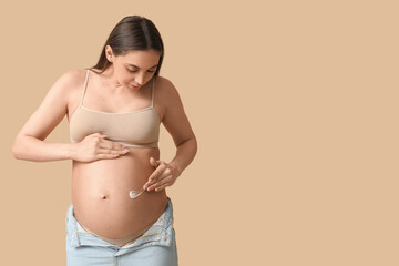 Young pregnant woman with cream against stretch marks on beige background