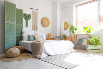 Stylish interior of light bedroom with comfortable bed and macrame on wall