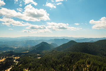 Fototapeta premium Panorama of beautiful nature aerial view white clouds, blue sky, horizon, mountains, pine forest and meadows. Nature. Relax