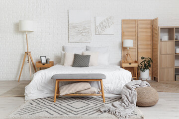 Stylish interior of light bedroom with comfortable bed, lamp and wooden folding screen