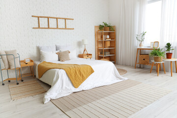 Stylish interior of bedroom with big comfortable bed and stepladder on white brick wall