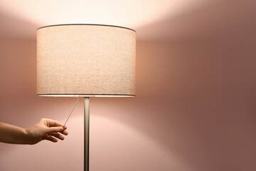 Woman turning on modern floor lamp on pink background