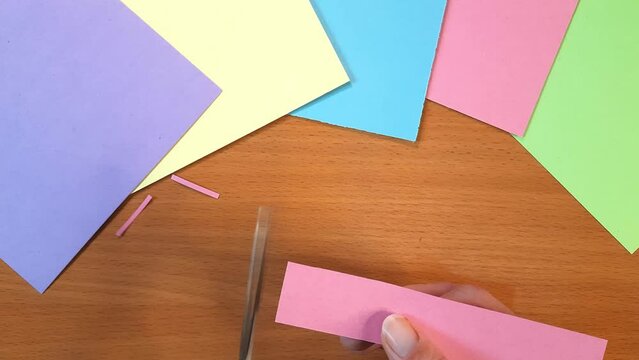 Woman making blanks for scrapbooking or collage or application or preschool art lesson. Person left-handed cutting pink paper into thin strips. Hands close up. handmade paper Art class