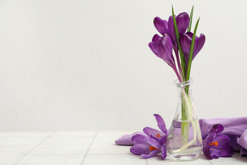 Glass vase with beautiful purple crocus flowers on white tile table