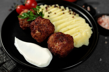 Fried cutlets with mashed potatoes, tomatoes and herbs. Black plate on a black background