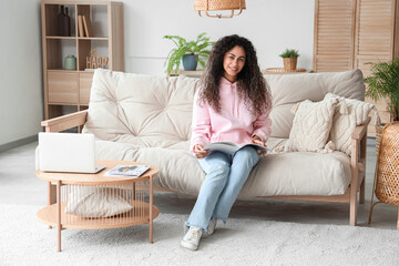 Obraz premium Young African-American woman reading magazine on sofa at home