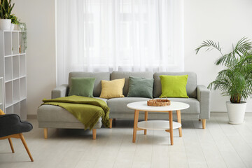 Stylish living room with comfortable sofa, coffee table, shelving units and curtains