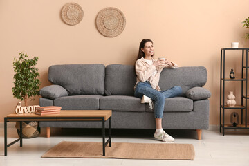 Young woman holding cup and sitting on sofa in stylish living room