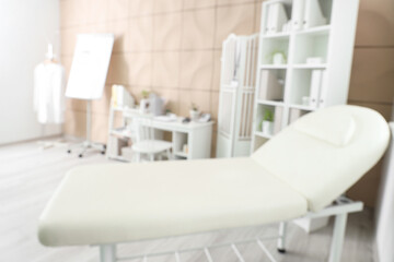 Blurred view of medical office with couch, doctor's workplace and shelf units