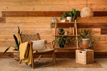 Shelving unit with houseplants and armchair near wooden wall in living room