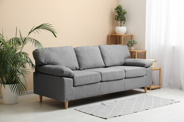 Stylish living room with black sofa, shelving unit and houseplants near beige wall