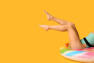 Young woman in stylish swimsuit lying on inflatable mattress against yellow background