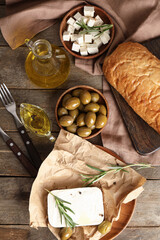 Plate with tasty feta cheese, olives, rosemary and peppercorn on wooden background