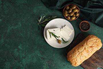 Plate with tasty feta cheese, rosemary and olive on green background