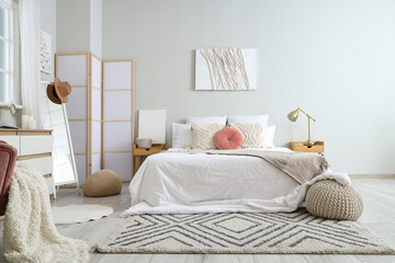 Stylish bedroom room with white bed, folding screen, bedside tables and picture