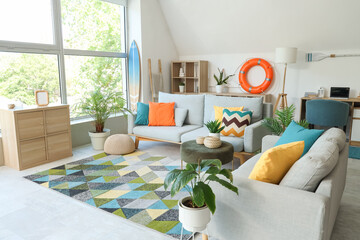 Comfortable sofas, pouf and surfboard in interior of living room