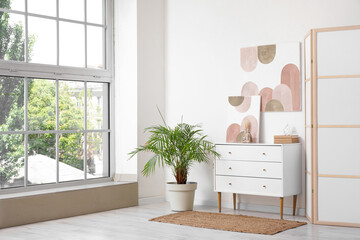 Stylish room with chest of drawers, houseplant and picture on white wall