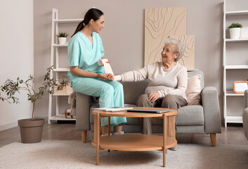 Senior woman with physical therapist bandaging her arm at home