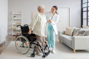 Physical therapist helping senior woman to stand up from wheelchair at home