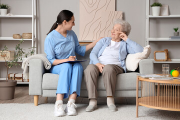 Obraz premium Senior woman with physical therapist writing in clipboard on sofa at home
