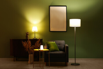 Glowing lamps on chest of drawers, armchair and picture in stylish living room