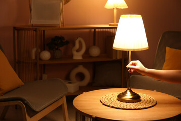 Female hand turning on lamp on coffee table in stylish living room, closeup