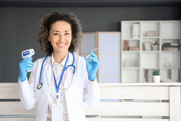 Mature female doctor with infrared thermometer and syringe in clinic