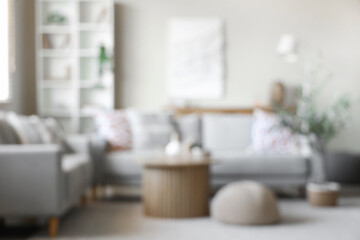 Interior of stylish living room with cozy sofa, shelving unit, coffee table and olive tree, blurred...