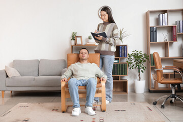 Female psychologist with notebook and hypnotized man in office
