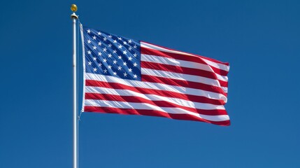 Fototapeta premium The United States flag features stars and stripes, representing the 50 states and 13 original colonies, waving in the wind against a clear blue sky