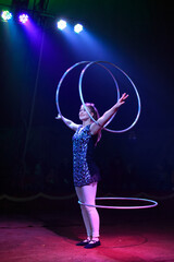 Young slim attractive circus gymnast woman performing live show with hula hoops on red arena with...