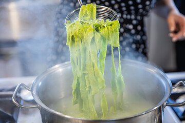 Spinach Green Pasta. Spinach pasta. Female chef throws green spinach pasta dough into a boiling pot...