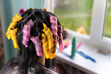 A woman with long black hair gets her hair styled with pink and yellow curlers