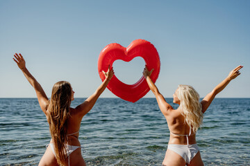 Two women are holding a red heart shaped inflatable raft in the ocean