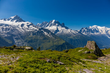 Tour du Montblanc beautiful mountain ladscapes of the Alps green valley, snow summit of Montblanc and rocky peaks of Aiguille du Midi in summer sunny weather blue sky, trekking and hiking in Chamonix