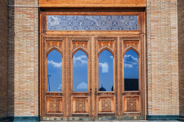 Obraz premium old carved wooden door with glass with Uzbek pattern to the ancient Islamic Mosque of Hazrati Imam in Uzbekistan