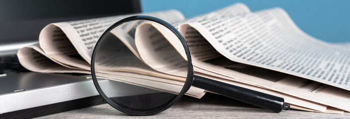 Newspapers on laptop and magnifying glass, news, information concept, media