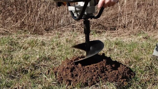 Drilling the ground with rig machine. The man drills the hole in land. Borering for the fence installation. Bore tool. Handy equipment. Portable manual earth auger for planting bushes and trees. 4K