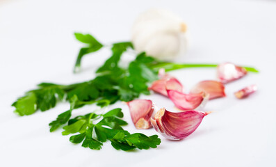 Cutting board with fresh seasonings on a wooden background. White garlic heads and cloves and parsley leaves. Condiments