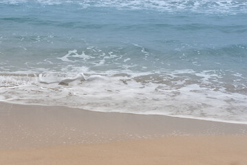 Background of waves flowing gently onto the beach. You can see the beach, the waves with foam and the blue sea. There is space for text.