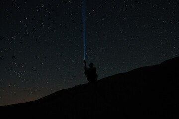 Man shines lantern in the sky. man with flashlight point to the starry sky at midnight. - Powered by Adobe