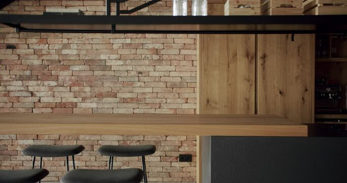 Modern and spacious wooden kitchen room with wall bricks and black staircase. Real Estate. Luxury kitchen with wooden island and chairs. Minimalist design in New Home. Neoclassic Style, cozy interior.
