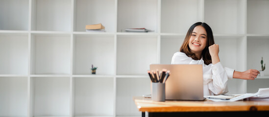 Young woman smiling and stretching while working from home at a desk with a laptop and office...