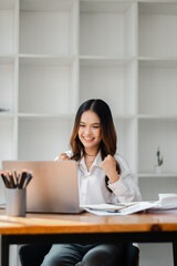 A young woman in a white shirt celebrates success while working on a laptop in a modern office with...