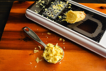 Tablespoon of Grated Ginger with a Grater: A measuring spoon of grated ginger on a wooden cutting...