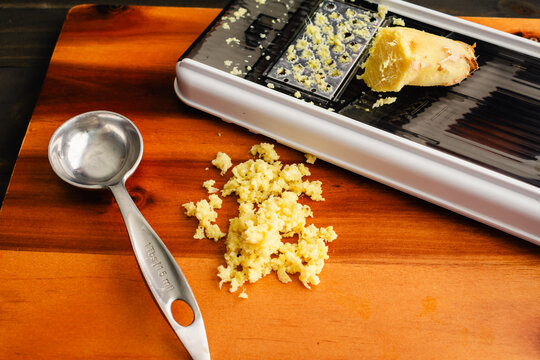 Grated Ginger with a Grater: A tablespoon of grated ginger on a wooden cutting board with a mandoline