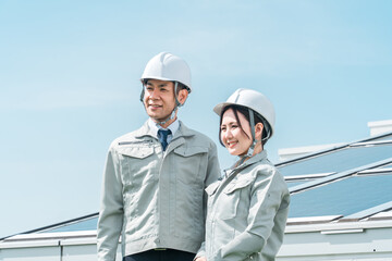 太陽光発電・ソーラーパネルの前に立つ電力会社・電気工事業者の作業着姿の技術者・ビジネスパーソン
